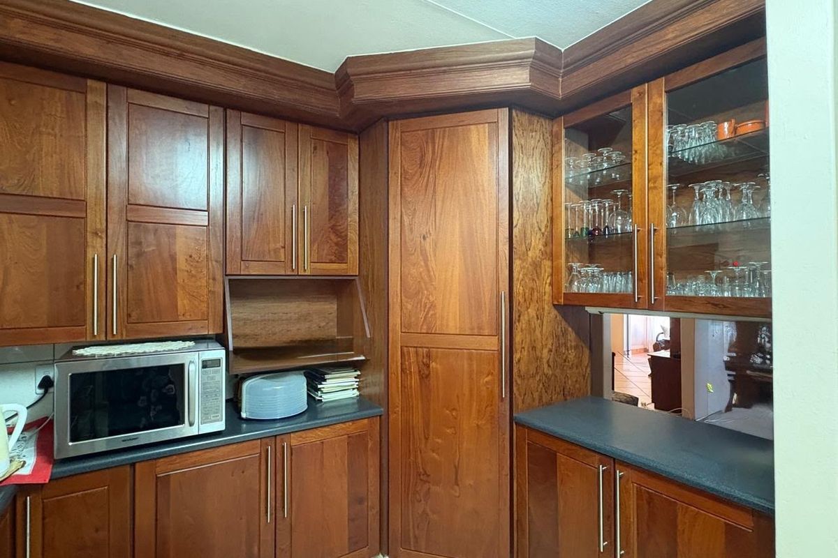 A well-maintained kitchen featuring rich wooden cabinetry, dark laminate countertops, and glass-front display units with integrated crown molding.