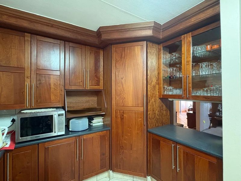 A well-maintained kitchen featuring rich wooden cabinetry, dark laminate countertops, and glass-front display units with integrated crown molding.