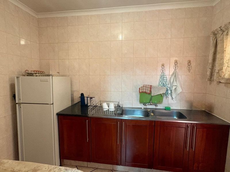A functional scullery area featuring a double stainless steel sink, dark laminate countertops, and wooden cabinetry with tiled splashback walls.