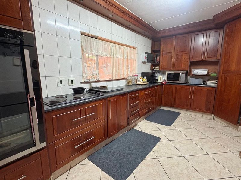 A functional kitchen featuring extensive wooden cabinetry, built-in oven, electric hob, tiled backsplash, and ceramic floor tiles.
