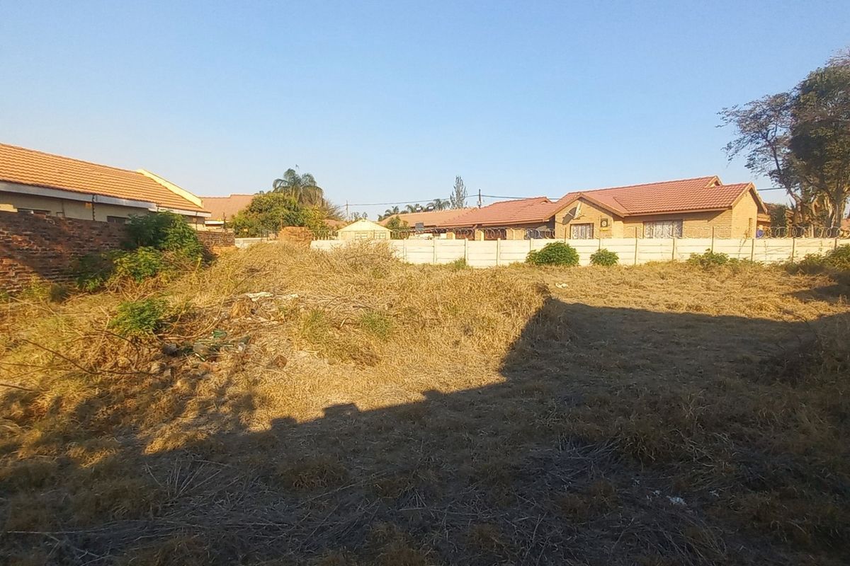 A vacant residential plot featuring perimeter brick and precast concrete boundary walls with installed electric fencing, currently covered in dry, overgrown vegetation.