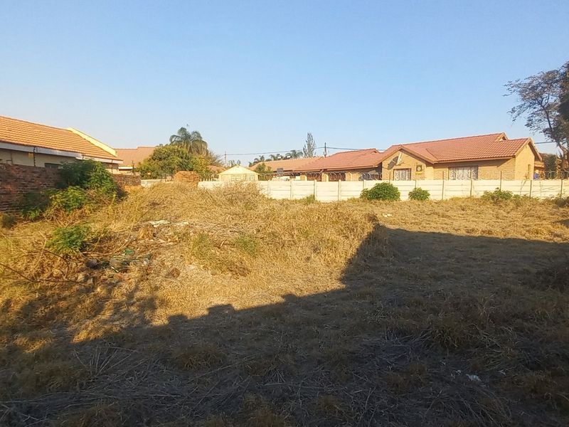 A vacant residential plot featuring perimeter brick and precast concrete boundary walls with installed electric fencing, currently covered in dry, overgrown vegetation.