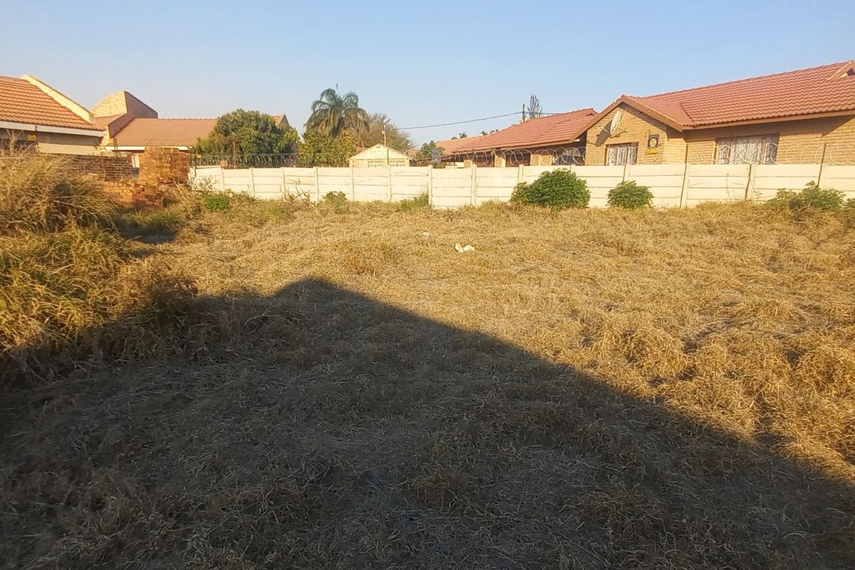 A vacant residential plot featuring a precast concrete boundary wall with security razor wire, surrounded by established residential properties.