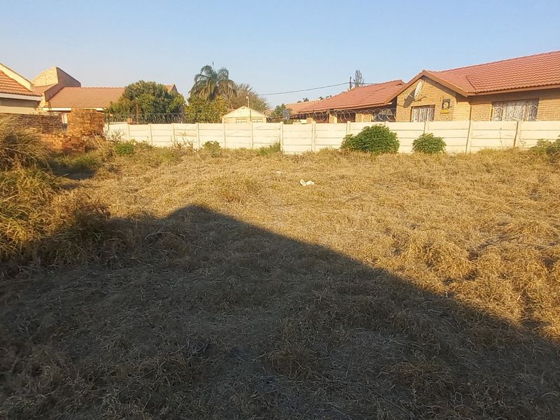 A vacant residential plot featuring a precast concrete boundary wall with security razor wire, surrounded by established residential properties.