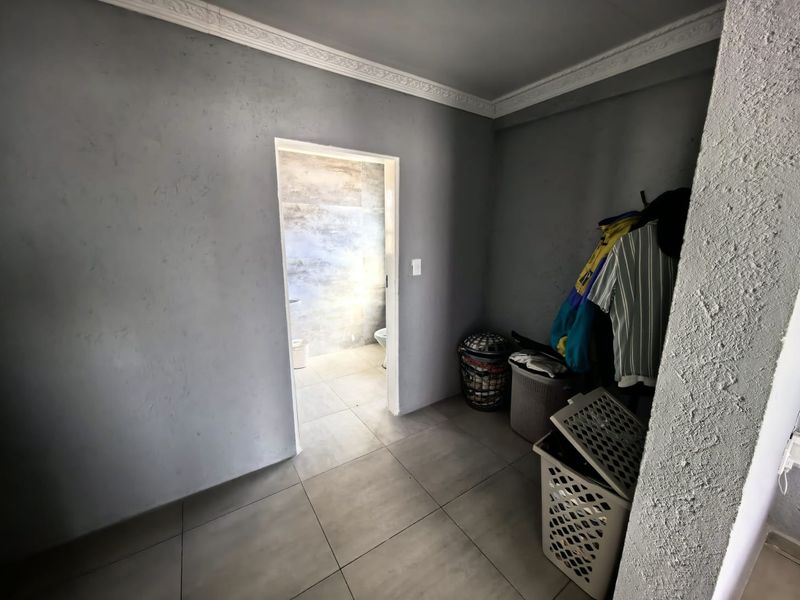 A neutral-toned hallway featuring crown molding and large format floor tiles, providing access to an adjacent tiled bathroom area.
