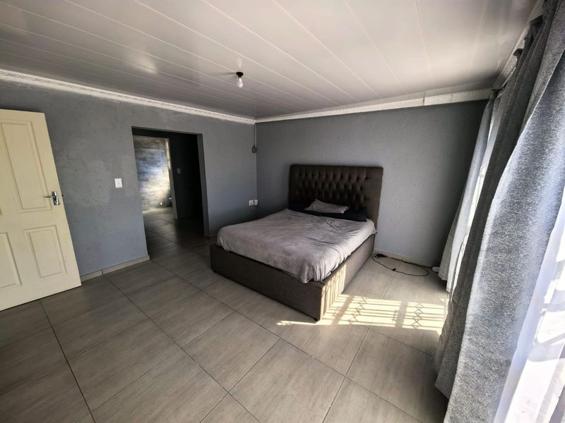 A spacious bedroom featuring tiled flooring, a panelled ceiling with coving, and direct access to an adjoining room.