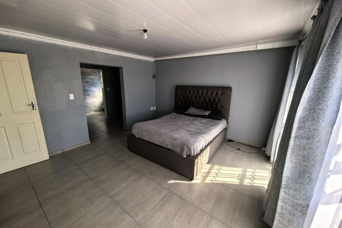 A spacious bedroom featuring tiled flooring, a panelled ceiling with coving, and direct access to an adjoining room.