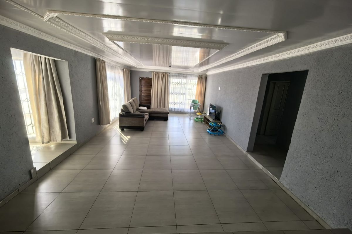Spacious living room featuring large format floor tiles, decorative ceiling molding, and a recessed ceiling design with natural light from large windows.
