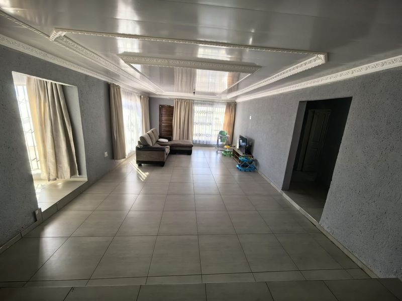Spacious living room featuring large format floor tiles, decorative ceiling molding, and a recessed ceiling design with natural light from large windows.