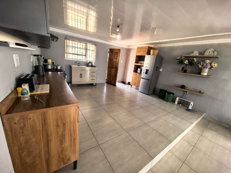 A functional kitchen area featuring tiled flooring, built-in cabinetry, a sink, and an extractor fan, with a raised floor section and direct exterior access.