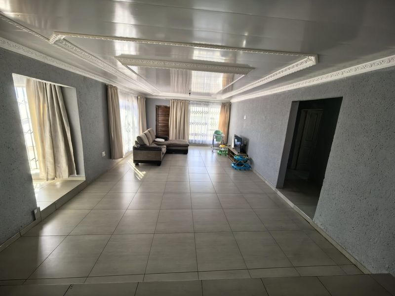 Spacious living room featuring large format floor tiles, textured grey walls, and decorative ceiling molding with a glossy finish.
