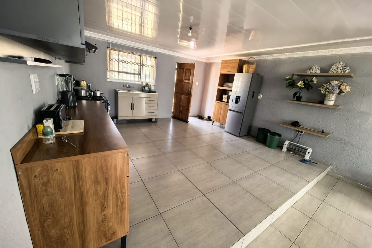 A functional kitchen area featuring tiled flooring, built-in cabinetry, a stainless steel sink, and an extractor fan, with direct access to an exterior door.