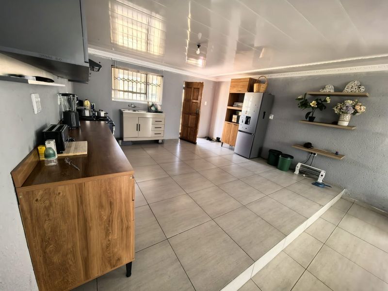 A functional kitchen area featuring tiled flooring, built-in cabinetry, a stainless steel sink, and an extractor fan, with direct access to an exterior door.