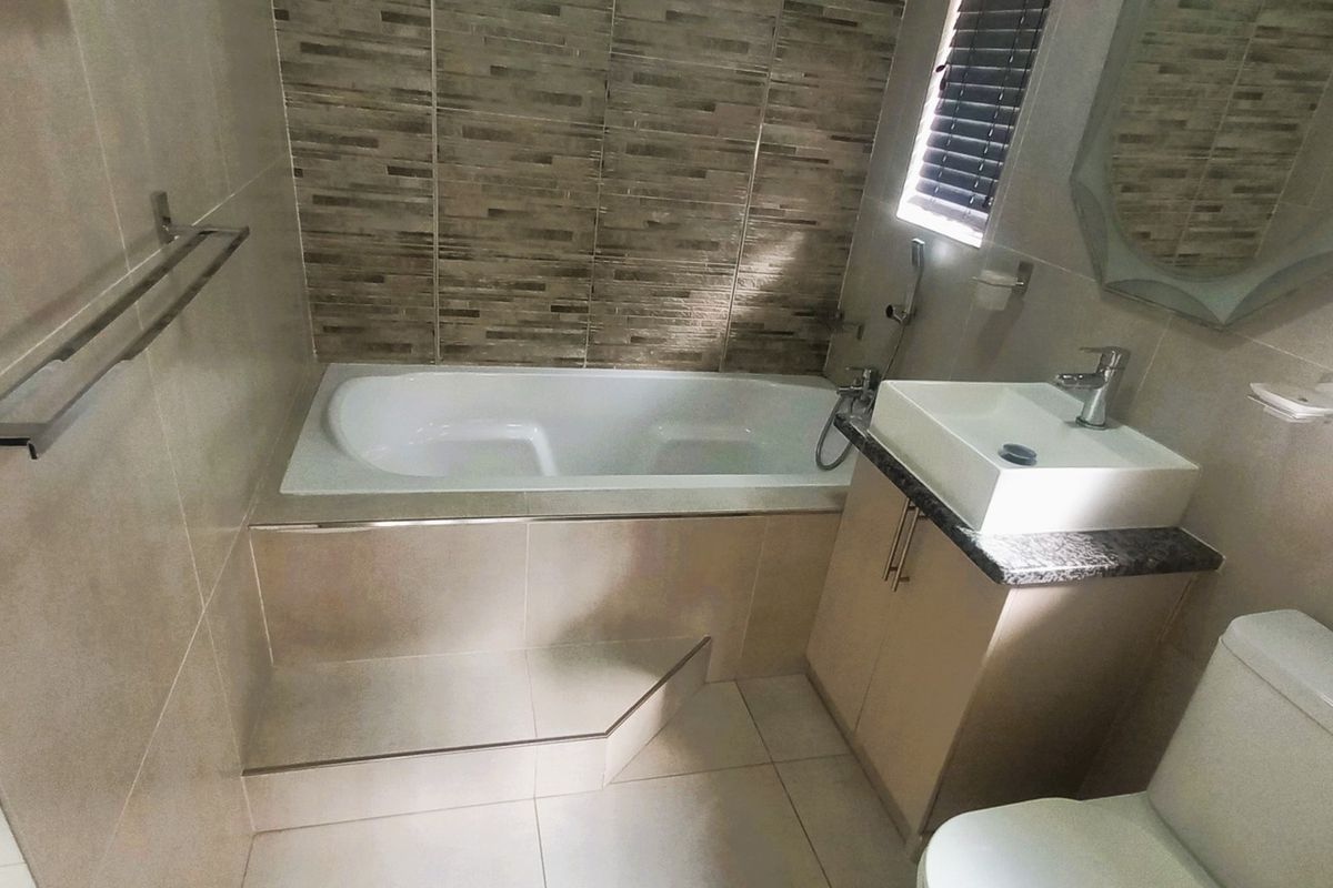 Modern bathroom featuring a built-in bathtub, vessel sink with vanity cabinet, toilet, and neutral tiled finishes.
