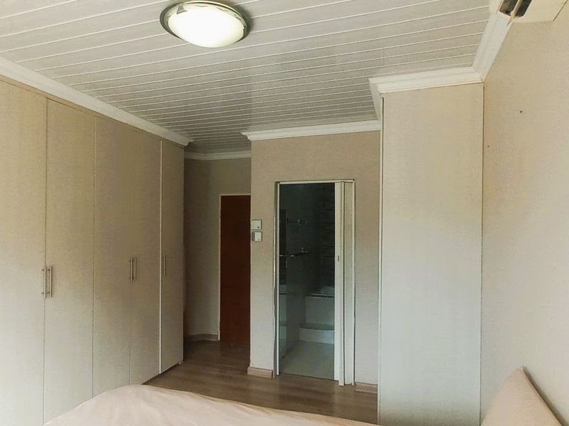 Bedroom featuring extensive built-in cupboards, laminate flooring, and direct access to an en-suite bathroom.