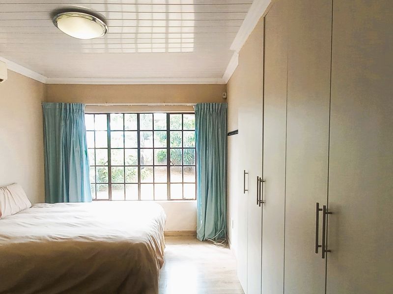 A bedroom featuring built-in cupboards, timber-look flooring, a tongue and groove ceiling, and an air conditioning unit.
