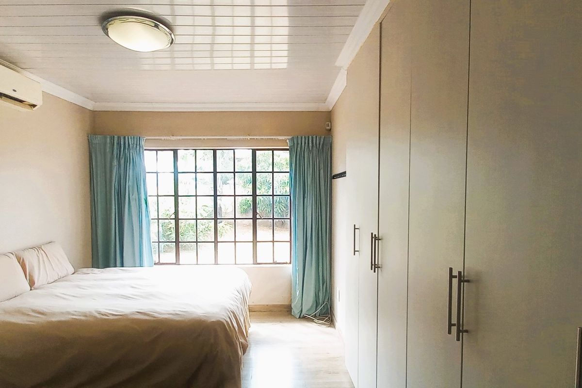 A bedroom featuring built-in cupboards, timber-look flooring, a tongue and groove ceiling, and an air conditioning unit.