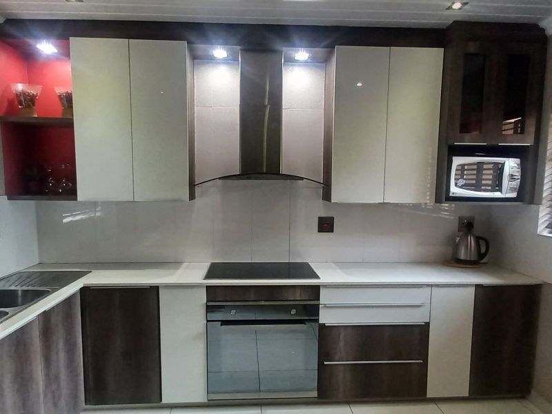 Modern kitchen featuring two-tone cabinetry, integrated appliances including an oven, hob, and microwave, double sink, and tiled splashback with recessed lighting.