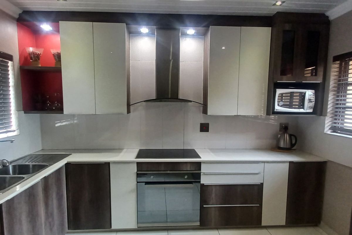 Modern kitchen featuring two-tone cabinetry, integrated appliances including an oven, hob, and microwave, double sink, and tiled splashback with recessed lighting.