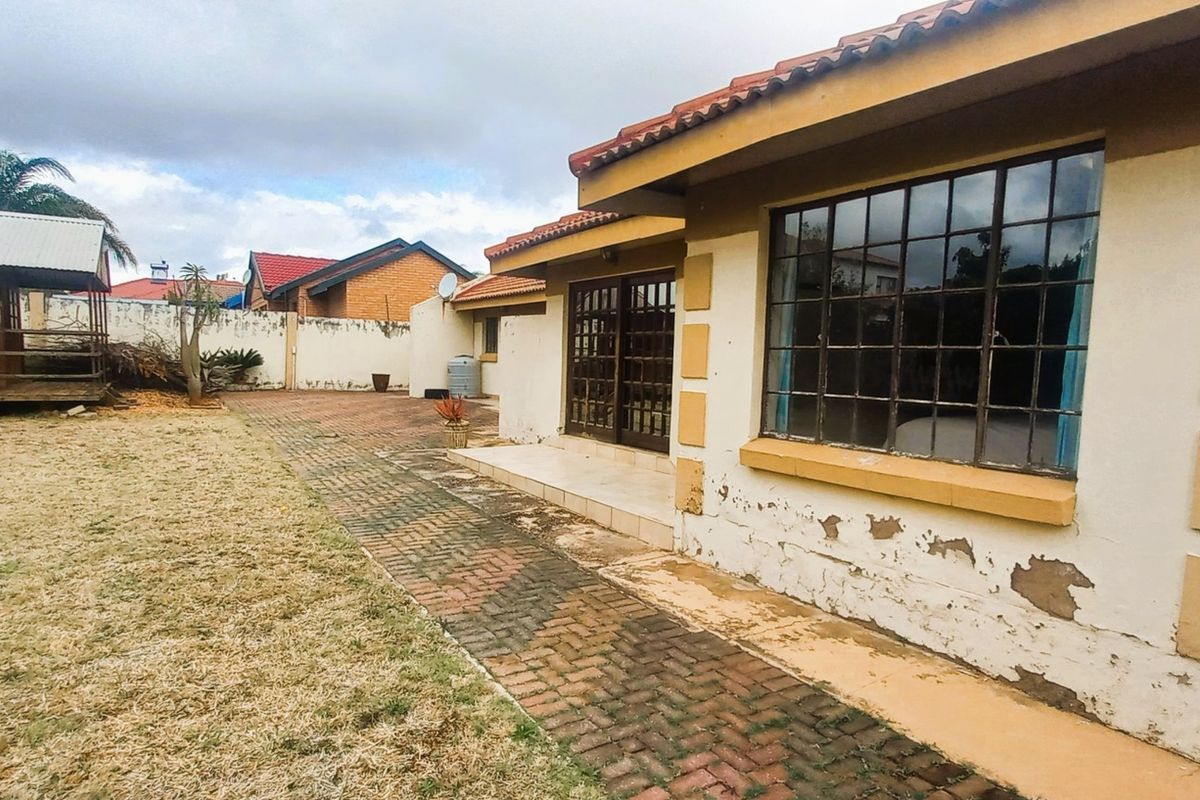 Rear view of the property featuring a paved patio area, sliding door access, and a garden with a detached wooden structure.