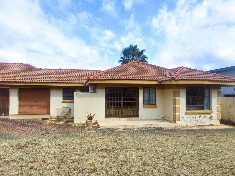 Rear view of a single-story house featuring a terracotta tiled roof, paved driveway, and a perimeter wall with electric fencing.