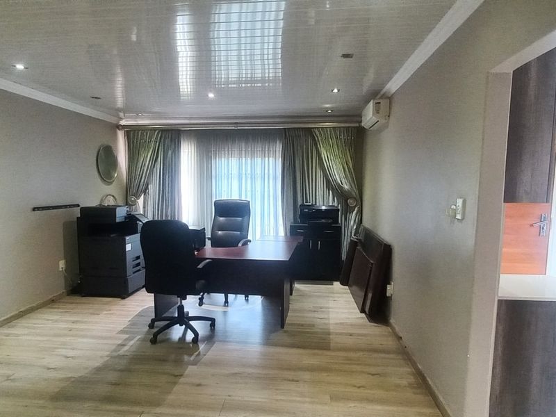 A spacious office area featuring laminate flooring, recessed ceiling lighting, and a wall-mounted air conditioning unit.