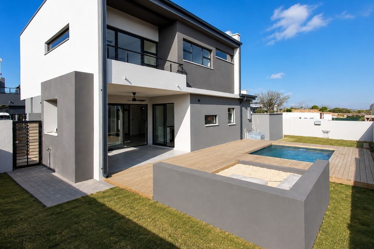 Modern double-story home featuring a rear patio, timber decking, swimming pool, and a balcony overlooking the landscaped garden.
