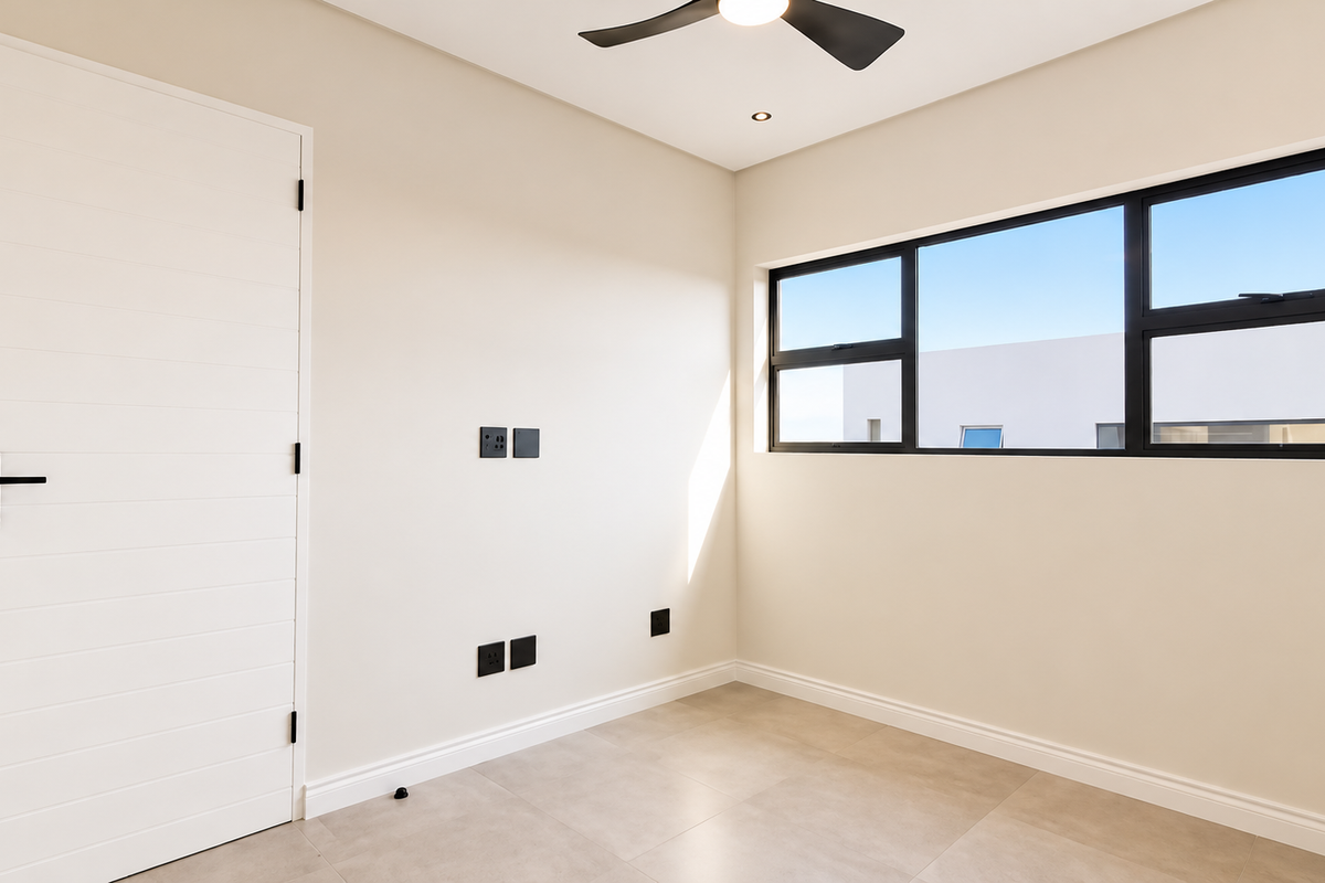 A bright, modern, and empty bedroom featuring neutral walls, tiled flooring, a ceiling fan, and large black-framed windows.