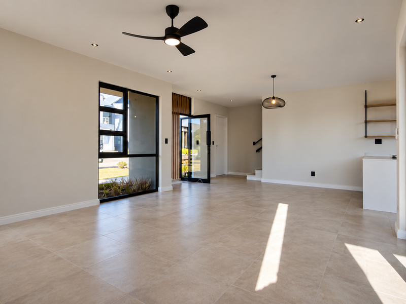 Spacious, modern open-plan living area featuring neutral tiled flooring, recessed lighting, a ceiling fan, and large black-framed windows and sliding doors for natural light.