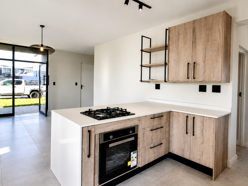 Modern kitchen featuring light wood-finish cabinetry, stone countertops, built-in oven, gas hob, and sleek track lighting, opening directly to an outdoor area.