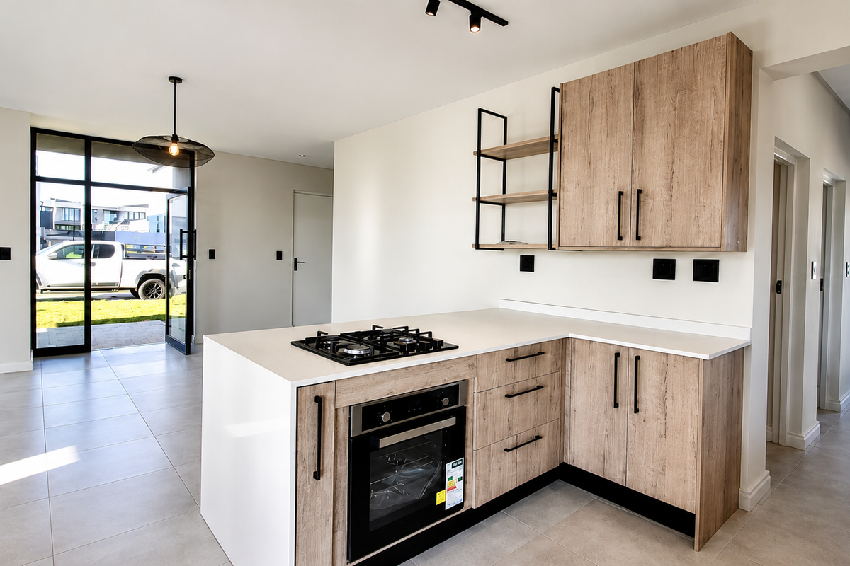 Modern kitchen featuring light wood-finish cabinetry, stone countertops, built-in oven, gas hob, and sleek track lighting, opening directly to an outdoor area.