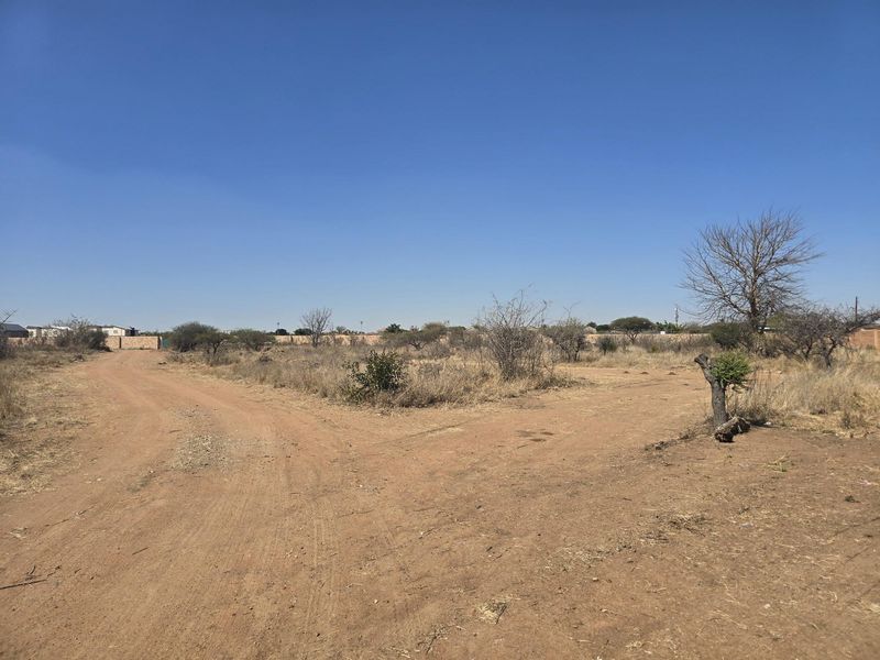 A view of a vacant residential plot featuring a dirt road access and surrounding boundary walls in a dry landscape setting.