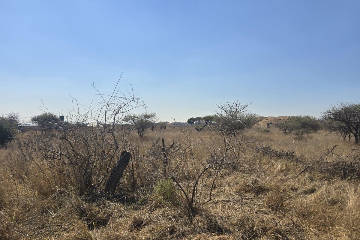 A view of the vacant residential land featuring dry grassland and native vegetation under a clear blue sky.