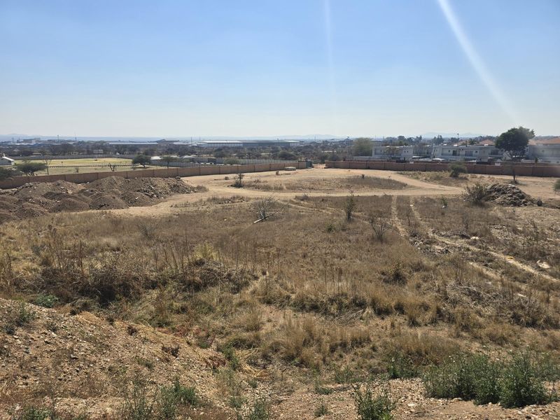 An elevated view of a vacant residential plot featuring dry vegetation and a perimeter boundary wall.