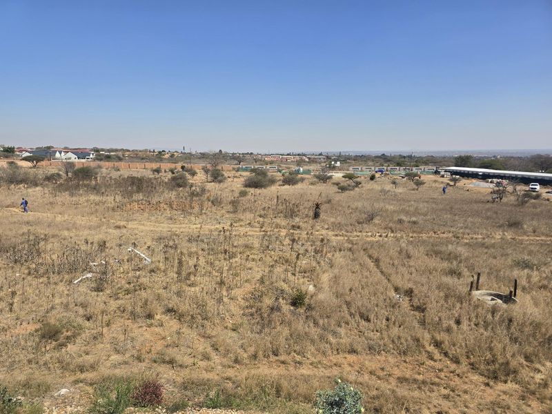 An elevated view of a large, undeveloped residential plot featuring natural dry vegetation and open space.