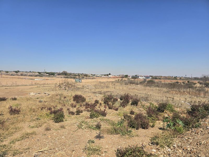 A wide-angle view of a vacant residential plot featuring natural vegetation and surrounding neighborhood landscape.
