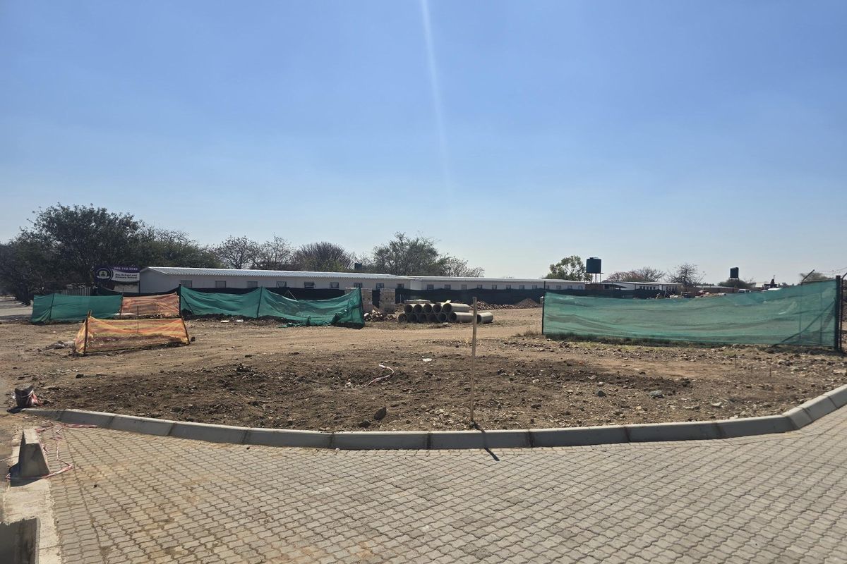 A vacant residential plot featuring paved driveway access, concrete curbing, and perimeter fencing, ready for development.