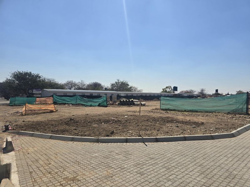 A vacant residential plot featuring paved driveway access, concrete curbing, and perimeter fencing, ready for development.