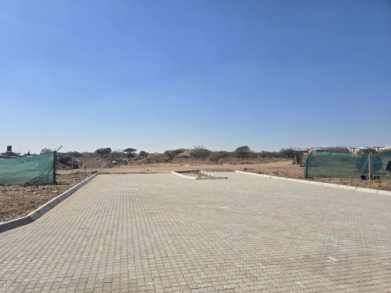 A clear view of a vacant residential plot featuring a newly paved driveway and concrete kerbing, ready for development.