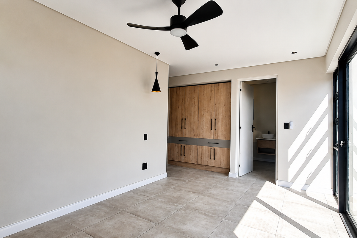 A bright, modern bedroom featuring neutral walls, tiled flooring, built-in wooden cabinetry, a ceiling fan, and large sliding glass doors leading outdoors.