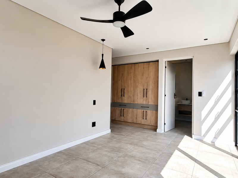 A bright, modern bedroom featuring neutral walls, tiled flooring, built-in wooden cabinetry, a ceiling fan, and large sliding glass doors leading outdoors.