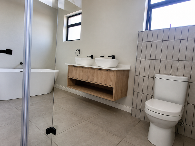 Modern bathroom featuring a freestanding bathtub, double vessel sink vanity with wood finish, and a tiled feature wall with a toilet.