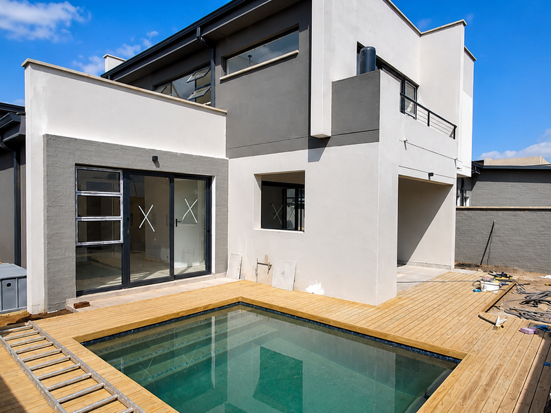 Modern rear exterior featuring a swimming pool with timber decking, sliding glass doors, and a contemporary two-story facade under construction.