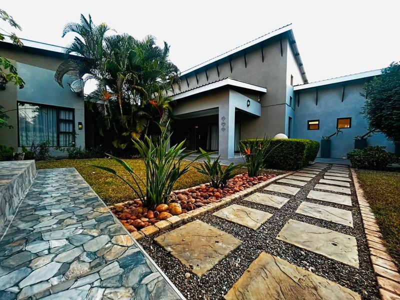 A well-maintained rear exterior view featuring a landscaped garden, stone-paved pathways, and a covered patio area attached to the main house structure.