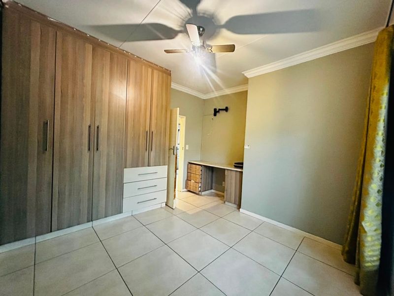 A spacious bedroom featuring extensive built-in cupboards, a dedicated built-in desk area, tiled flooring, and a ceiling fan.