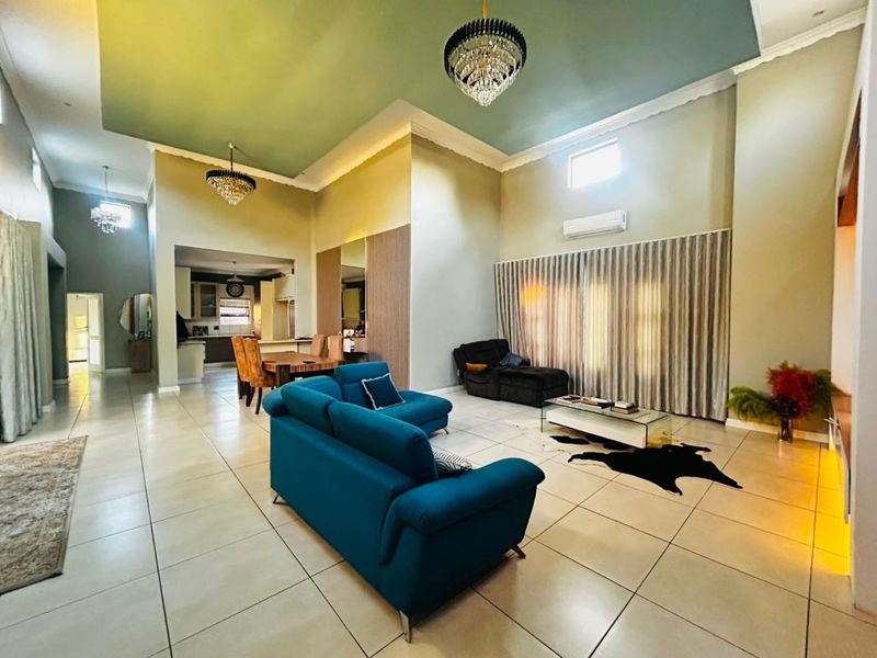 Spacious open-plan living and dining area featuring high ceilings with recessed lighting, crystal chandeliers, tiled floors, and an integrated kitchen space.