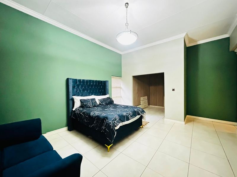 Spacious bedroom featuring tiled flooring, built-in cupboards, and a modern pendant light fixture with a feature green accent wall.