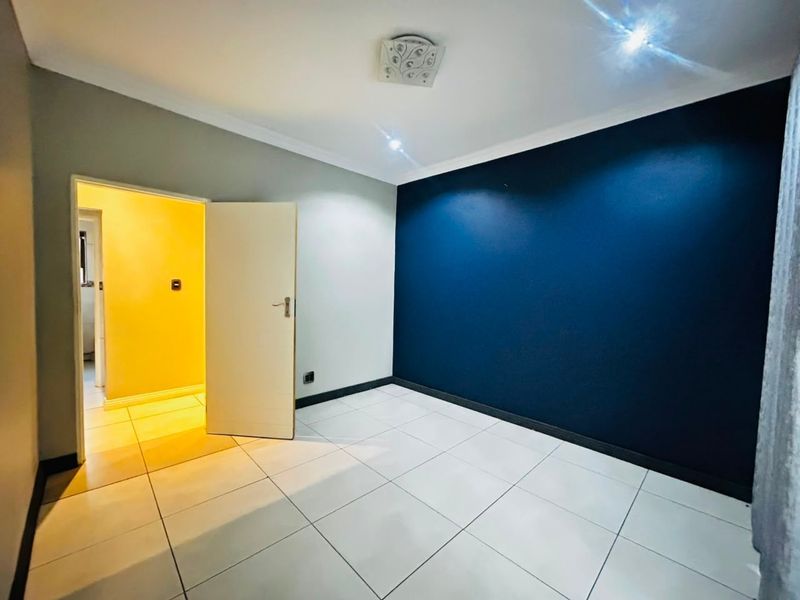 A bright, empty bedroom featuring neutral tiled flooring, a bold navy accent wall, and modern ceiling lighting fixtures.