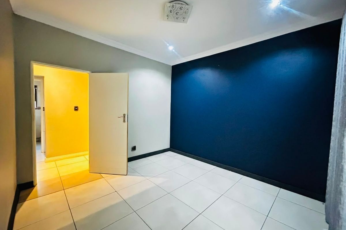 A bright, empty bedroom featuring neutral tiled flooring, a bold navy accent wall, and modern ceiling lighting fixtures.