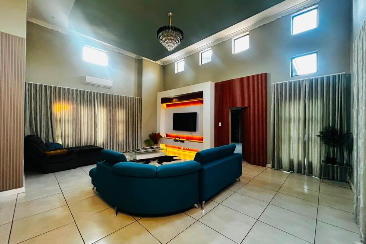 Spacious living room featuring high ceilings, tiled flooring, a modern built-in media unit with integrated lighting, and large windows with floor-to-ceiling curtains.